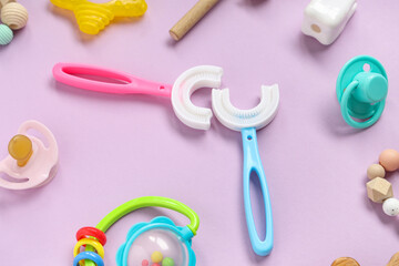 Children's toothbrushes with pacifiers and toys on lilac background