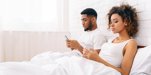 Couple in bed using smartphones separately at home