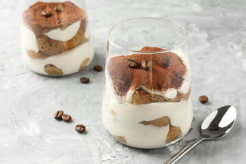 Delicious tiramisu in glasses, coffee beans and spoon on grey textured table