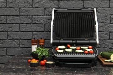 Electric grill with vegetables and spices on black marble table