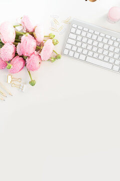Flat lay home office workspace - modern keyboard with ranunculus flowers, copy space on white background