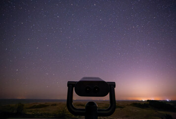 Telescope on the beach at night with stars in the sky