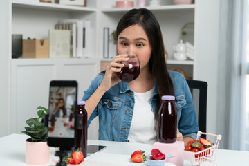 Smiling young beautiful Asian reviewing tasty mixed strawberry and cherry juice detox drinks,...