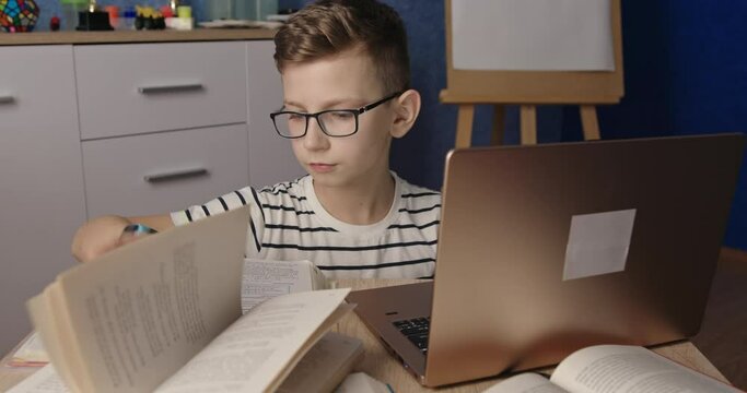 A young boy is seated at a table with a laptop and book