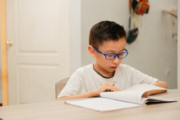 Concentrated Hispanic boy doing homework at home - boy writing in his notebook studying from home. Education or back to school concept