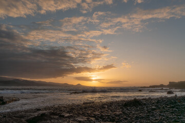 Orange sky at sunset on a beach of pebbles and volcanic rocks