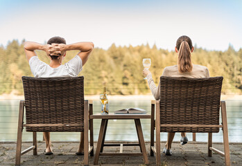 Young couple on holiday vacation relaxing drinking wine reading and enjoying beautiful nature lake...