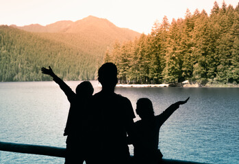 Family father children with  arms outstretched on a mountain lake at sunrise enjoying freedom and...