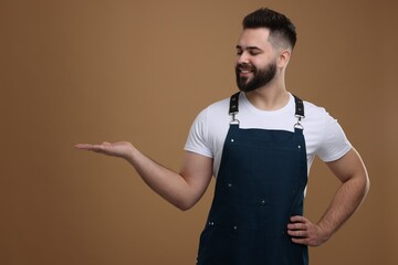 Smiling man in kitchen apron holding something on brown background. Mockup for design
