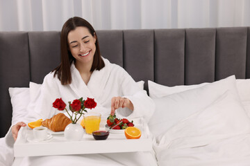 Obraz na płótnie Canvas Smiling woman having breakfast in bed at home, space for text
