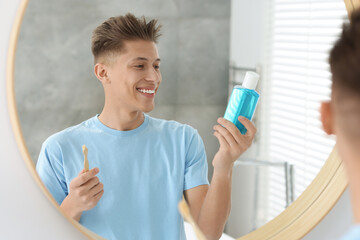 Young man with mouthwash and toothbrush near mirror in bathroom