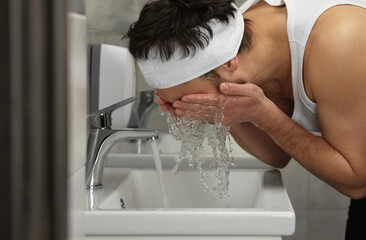 Man with headband washing his face in bathroom