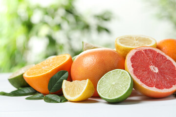 Different fresh citrus fruits and leaves on white table against blurred background, closeup
