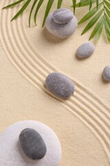 Zen garden stones and green leaves on sand with pattern, flat lay