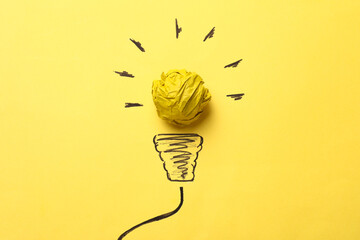 Idea concept. Light bulb made with crumpled paper and drawing on yellow background, top view