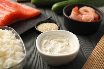 Cream cheese in bowl and other ingredients for sushi on black wooden table, closeup