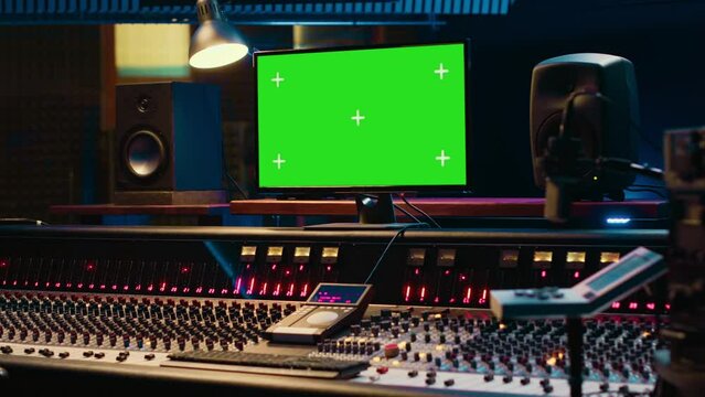 Empty professional studio showing greenscreen layout on monitor, mixing console with a variety on buttons, knobs and sliders. Audio engineering control room with technical gear. Camera A.