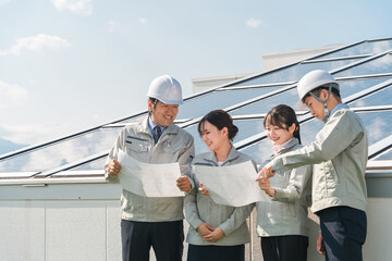 太陽光発電・ソーラーパネルの前に立つ電力会社・電気工事業者の作業着姿の技術者（クリーンエネルギー）
