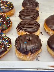 Close-up of delicious chocolate glazed doughnuts with sprinkles in a bakery display