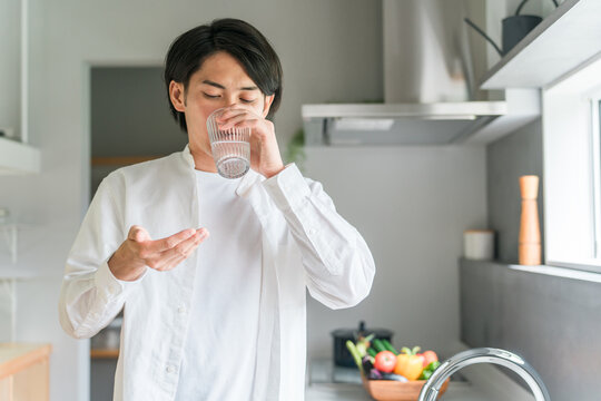 キッチンで内服薬・サプリ・医薬品を飲む病気の男性・投薬
