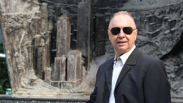 A man wearing sunglasses stands in front of a large statue of a city
