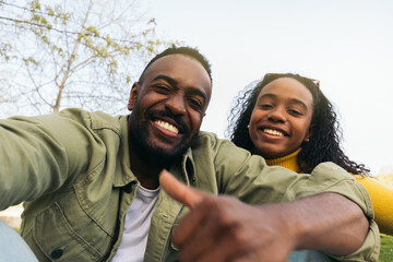 afro american couple taking a selfie sitting in a park