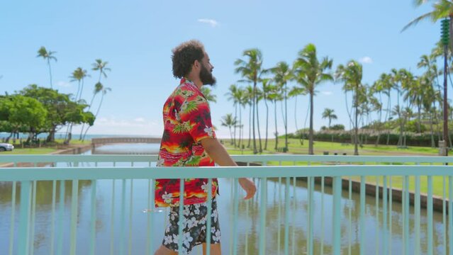 Happy male tourist in colorful Hawaiian outfit spending wonderful time in vacation on Hawaii island, Oahu, strolling in park on a sunny day, waving hello. High quality 4k footage