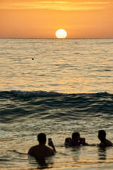 A family swims in the sea against the background of the setting sun