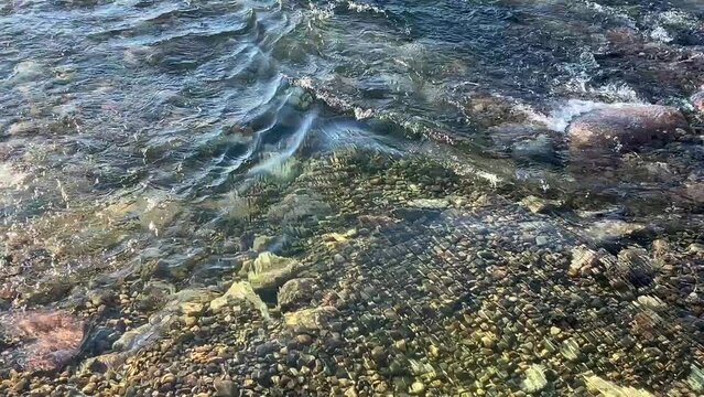Clear river shines in sun as it flows over rocks and pebbles