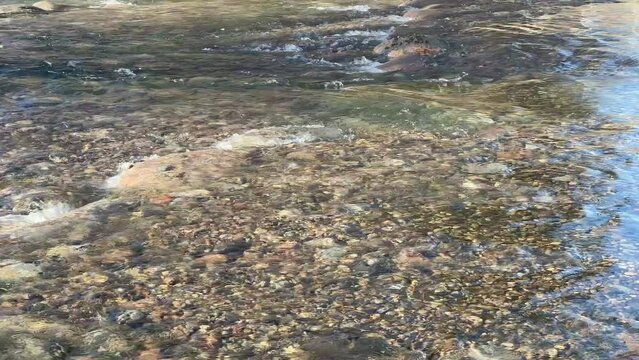 Closeup of clear river flowing across rocky rapids