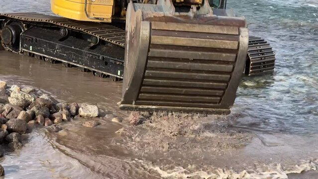 Closeup of backhoe moving around in a rocky river
