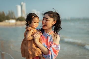 happy mother holding and talking toddler baby girl on sea beach