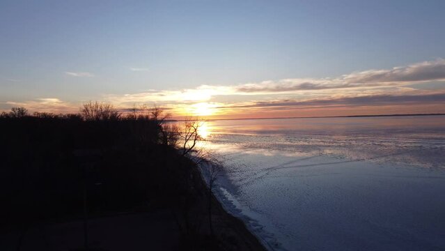 Aerial pan up a winter sunset reflecting on frozen lake