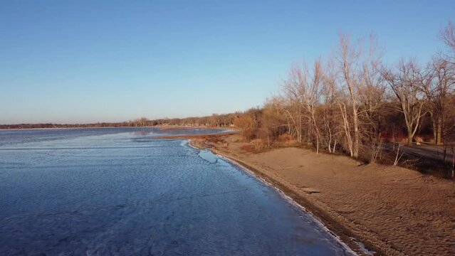 Aerial flyover of sandy beach on a frozen lake in early winter