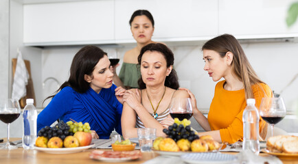 Obraz na płótnie Canvas At cozy home gathering, attentive female friends comforting and supporting upset woman, discussing problems and giving advice over glass of wine