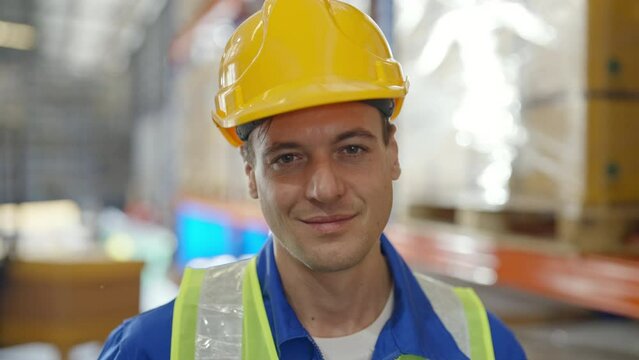 Handsome man and happy professional worker wearing safety vest and hard hat, Smiling to camera. Big warehouse with shelves full of stock
