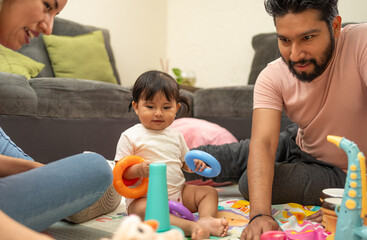 Hispanic father, mother, and baby daughter bonding in the living room, engaging in learning and...
