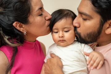 hispanic couple kissing daughter, young latin couple with a baby girl toddler