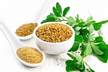 Fenugreek in bowl and two spoons with leaves on white board - obrazy, fototapety, plakaty