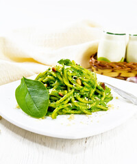 Spaghetti with spinach and pine nuts in plate on wooden board