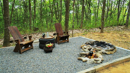 Two rock fire pit with wood table and chairs on gravel floor in the garden background. Stone fire...
