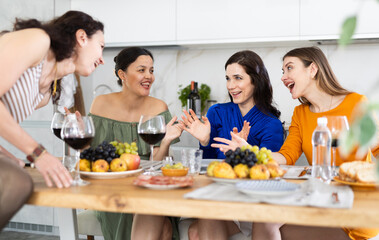 Happy women congregated around a festive table; participating in animated discussions and enjoying the delights of red wine