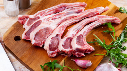 Raw hogget chops on ribs on wooden board with fresh fragrant arugula leaves, garlic and seasonings....