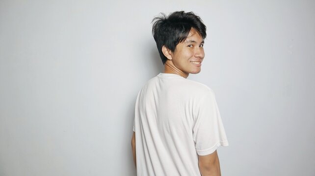 Asian young man smiling posing from his back looking forward as if turning his body