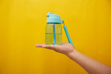 Female hand holding a blue water bottle for baby on yellow background