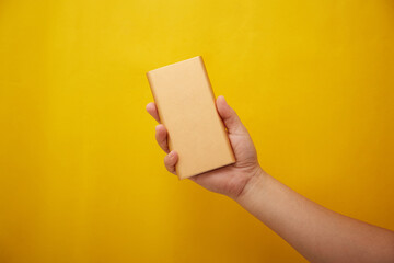 Photo of hand holding a power bank, external battery on yellow background