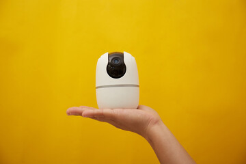 A hand hold a wireless security camera on yellow background 