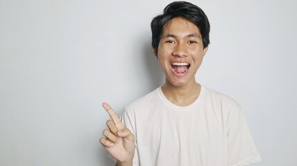 Excited young Asian man in white shirt pointing to the side