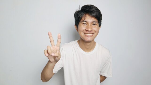 Happy young Asian man in white shirt forming a peace symbol with his hands