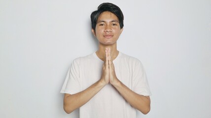 smiling young asian man in white shirt making traditional greeting gesture